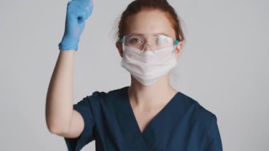Koruyucu gözlüklü, maskeli ve tıbbi eldivenli profesyonel kadın doktor, güvenle baş parmağını gösteriyor.