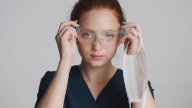 Beyaz arka planda koruyucu gözlük ve tıbbi maske takan çekici genç bir kadın doktor.