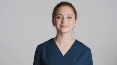 Genç, güzel, güler yüzlü doktor gri arka plandan kameraya bakıyor.