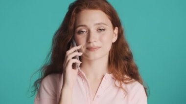 Güzel, çekici, kızıl saçlı kız telefonda mutlu bir şekilde konuşuyor ve renkli bir arkaplanda kameraya gülümsüyor.
