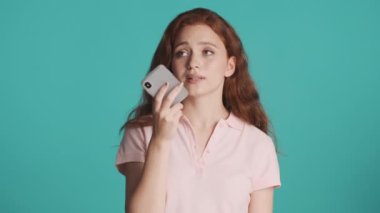 Çekici kızıl saçlı kız akıllı telefondan sesli mesaj kaydediyor. Renkli arka planda etrafa bakınıyor.