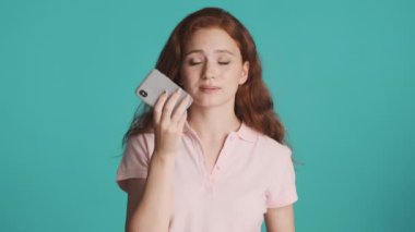 Güzel gülümseyen kızıl saçlı kız renkli arka plan üzerinden akıllı telefondan mutlu bir sesli mesaj kaydediyor.