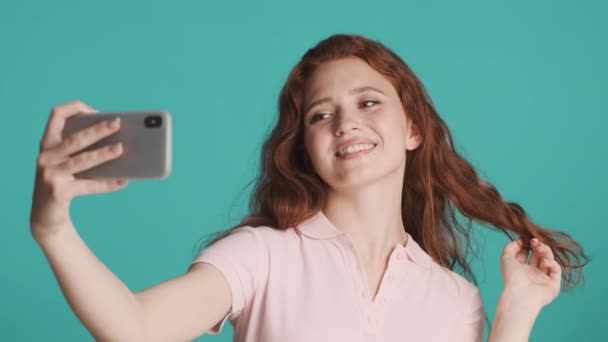 漂亮的红头发姑娘迷人地在智能手机上自私自利 在五彩缤纷的背景下高兴地在相机前摆姿势 — 图库视频影像