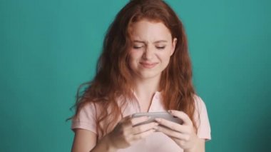 Oldukça heyecanlı kızıl saçlı kız renkli arka planda akıllı telefondan mutlu bir şekilde oyun oynuyor.