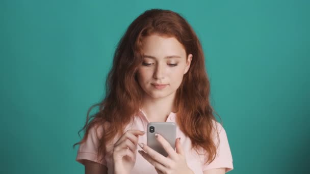 Chica Pelirroja Bastante Sorprendido Utilizando Teléfono Inteligente Sonriendo Sobre Fondo — Vídeo de stock