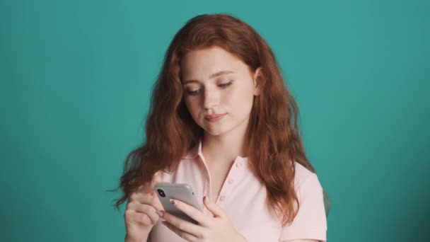 漂亮而自信的红头发女孩在五颜六色的背景下专注地使用智能手机 — 图库视频影像