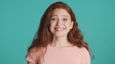 Kızıl saçlı kızın mutlu bir şekilde kameraya bakıp mavi arka planda gülümsemesine oldukça şaşırdım. Heyecanlı ifade