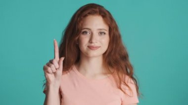 Güzel kızıl saçlı kız parmaklarıyla sayıyor ve renkli arka planda kameraların önüne atlıyor. Bir, iki, üç.