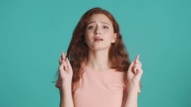 Tedirgin kızıl saçlı kızın portresi parmaklarını çapraz yapıp renkli bir arkaplan için kamera önünde dua ediyor. Lütfen ifade et