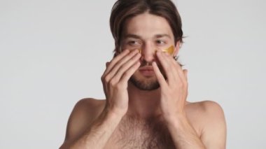 Çekici esmer adam beyaz arka plan üzerinden gözlerinin altına altın bantlar yapıştırıyor. Güzellik konsepti