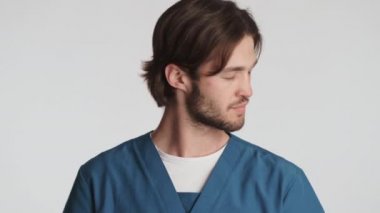 Genç ve çekici erkek doktor beyaz arka planda tıbbi maskesini çıkartıyor. Güvenlik kavramı