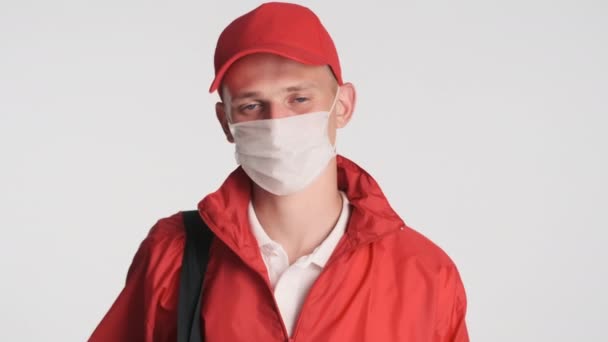 年轻迷人的送货员穿着红色制服 戴着医疗面具 高兴地把大拇指伸出来 安全概念 — 图库视频影像