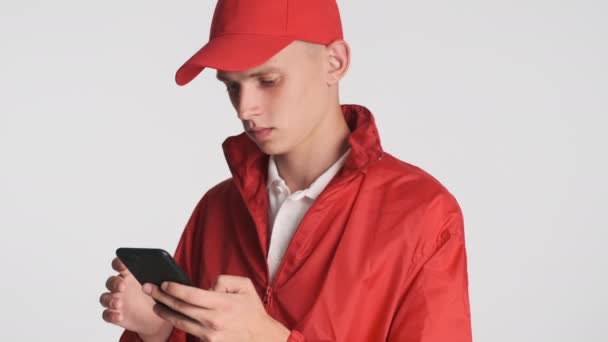 Portrét Mladého Atraktivního Kurýra Červené Čepici Bundě Zaujatě Pomocí Smartphonu — Stock video