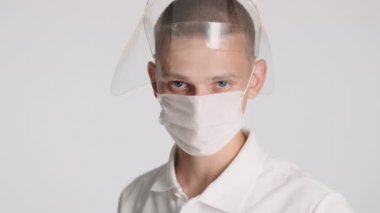Tıbbi maskeli çekici bir adamın portresi koruyucu maske takıyor ve güvenli bir şekilde izole edilmiş kameraya bakıyor. Önce güvenlik kavramı