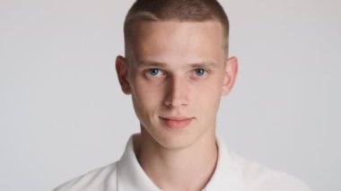 Çekici mavi gözlü adamın portresi kameraya bakıyor ve beyaz arka planda gülümsüyor.