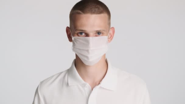 医療マスクの若いカジュアルな男が熱心に白い背景にカメラを見て 安全コンセプト — ストック動画