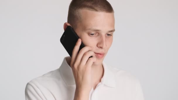 Mladý Pohledný Ležérní Muž Soustředěně Mluví Smartphone Přes Bílé Pozadí — Stock video