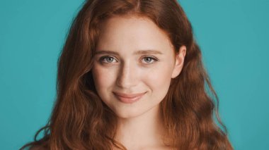 Güzel gülümseyen kızıl saçlı kızın portresi. Renkli arka planda kameraya şehvetle bakıyor.