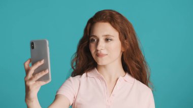 Çekici gülümseyen kızıl saçlı kız arkadaşlarıyla video görüşmesinde renkli arka planda akıllı telefon kullanıyor.