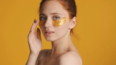 Altın göz bantları takan güzel bir kız renkli arka planda kameraya şehvetle poz veriyor. Güzellik konsepti