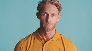 Genç, sarışın, sakallı bir adam kameraya bakıyor ve ne bileyim renkli bir arkaplanda nasıl bir ifade sergiliyor.