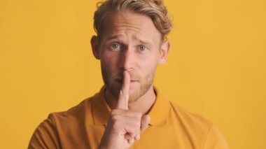 Çekici, gülümseyen, sakallı, sakallı bir adam. Renkli arka planda sessizlik jesti yapıyor. Gizli ifadeyi koru