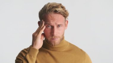 Genç, sarışın, sakallı adam beyaz arka planda şakaklarda acı gösteriyor.