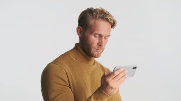 迷人的金发大胡子男人在白色背景下凝视着智能手机视频 — 图库视频影像