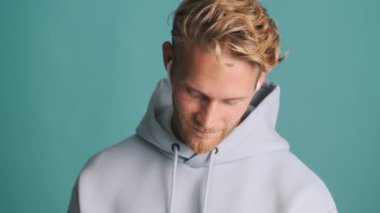 Çekici, şık, sarışın, kapüşonlu sakallı adam renkli arka planda kablosuz kulaklıkla müzik dinliyor.