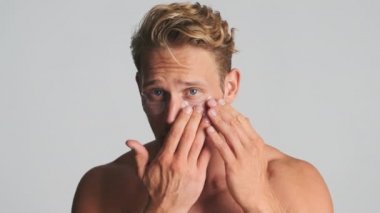 Yakışıklı sarışın sakallı adam mutlu bir şekilde göz bandı yapıştırıyor ve beyaz arka planda kameraya gülümsüyor.