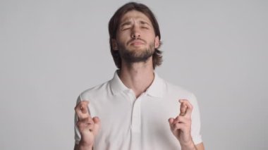 Gri arka plan için dua eden, parmaklarını çapraz yapmış genç duygusal bir adam. Lütfen ifade et