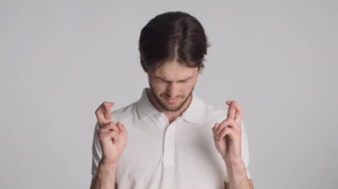 Parmaklarını çapraz yapıp dua eden, dua eden genç duygusal adam lütfen beyaz arka plan üzerinde hareket et.