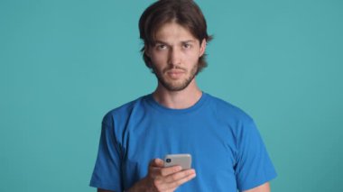 Çekici, ciddi sakallı, jest yapmayan, akıllı telefonu renkli arka planda kullanan bir adam.