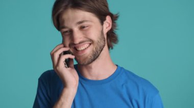 Yakından gülümseyen yakışıklı adam mavi arka planda telefonla konuşuyor.