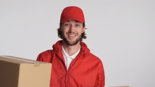 一个戴着红帽子的英俊的送货员用相机在白色背景上给纸板箱打趣地送东西 服务概念 — 图库视频影像