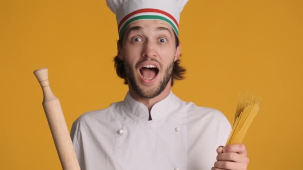 穿着制服 拿着滚动式别针和通心粉的英俊意大利厨师形象 在彩色背景下 在镜头前开心地微笑着 — 图库视频影像