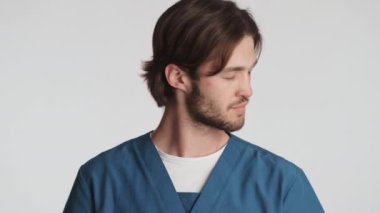 Genç ve çekici erkek doktor beyaz arka planda tıbbi maskesini çıkartıyor. Güvenlik kavramı
