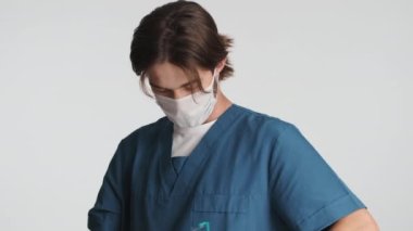 Genç çekici erkek doktor koruyucu gözlüklerini, tıbbi maskelerini ve eldivenlerini çıkarıyor ve beyaz arka planda mutlu bir şekilde gülümsüyor. Güvenlik kavramı