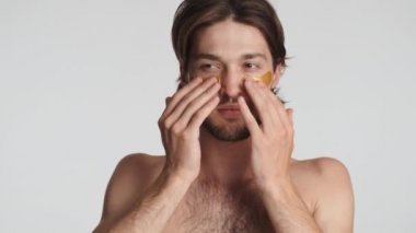 Çekici esmer adam beyaz arka plan üzerinden gözlerinin altına altın bantlar yapıştırıyor. Güzellik konsepti