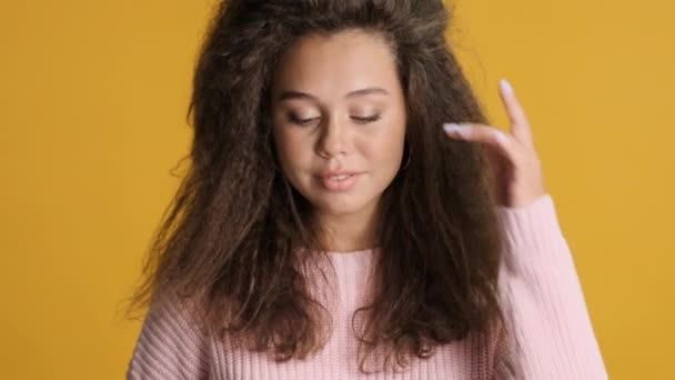 黄色の背景に可愛いポーズで巻き毛の魅力的なブルネットの女の子 薄情の感情 — ストック動画
