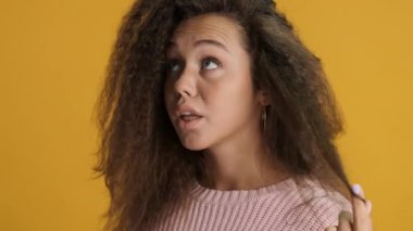 Dalgın esmer kız kıvırcık kıvrımlı düşünceli bir şekilde kamera önünde renkli bir arkaplanda poz veriyor