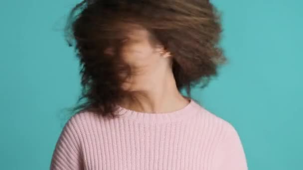 陽気なブルネットの女の子は彼女のふわふわの髪で遊んで カラフルな背景の上にカメラで笑顔 幸せな感情 — ストック動画