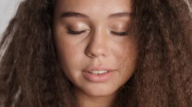 Çekici, tatlı esmer kız gözlerini açıyor ve mutlu bir şekilde kameraya gülümsüyor.