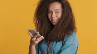 Güzel, gülümseyen esmer kız renkli arka plan üzerinden akıllı telefon kullanarak uzaktan iletişimden zevk alıyor. Çekici kız online alışveriş yapıyor.