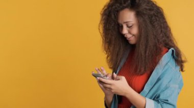 Güzel esmer kız arkadaşlarıyla internette sohbet ediyor fotokopi alanı yakınında sarı arka planda izole edilmiş akıllı telefon kullanıyor. Modern teknolojilerin aktif kullanıcısı
