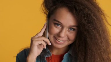 Güzel gülümseyen esmer kız, en iyi arkadaşıyla telefonda konuşuyor. Renkli arka planda kameraya bakıyor.