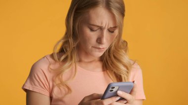 Sarı arka planda izole edilmiş erkek arkadaşından mesaj alamadığı için akıllı telefonu tutan mutsuz sarışın kız üzgün.