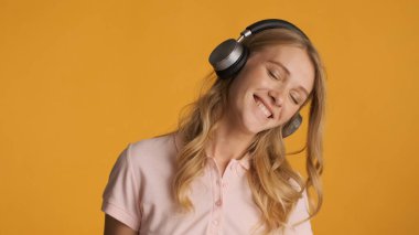 Güzel, gülümseyen sarışın kız sarı arka planda kulaklıkla yeni şarkılar dinliyor.