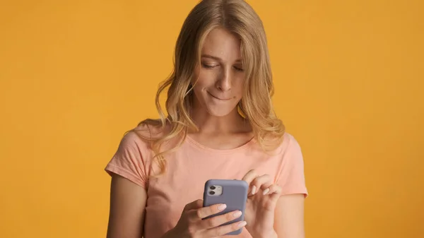 年轻的金发女人专注地阅读在黄色背景下隔离的智能手机上的信息 冲浪社交媒体 — 图库照片
