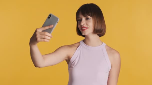 漂亮的黑发女孩 有着蓬乱的头发和红唇 在智能手机黄色背景下自拍 现代技术概念 — 图库视频影像